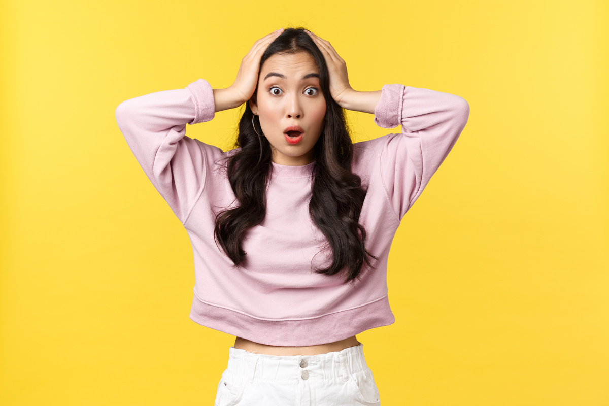 People Emotions, Lifestyle and Fashion Concept. Overwhelmed and Shocked Asian Girl Grab Head and React to concerning Big News, Saying Wow, Stare Camera Astonished, Yellow Background